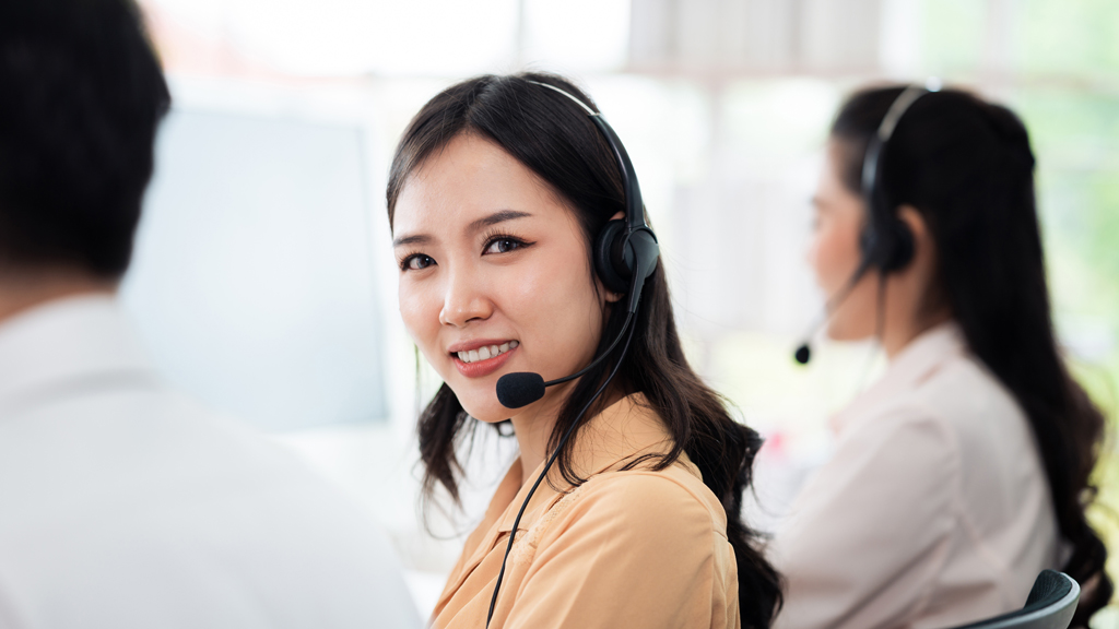 Team of call center staff in Asia wears headphones with a microphone. Smile while serving customers at desks and computers. Service concept and consulting. Communication concept.